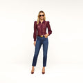 A woman wearing sunglasses, a maroon lace long-sleeve top, the Celestia Slim-Leg Jean in a dark indigo wash, and maroon heels poses against a plain white background with one hand in her pocket.