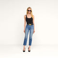 A woman wearing sunglasses, a black tank top, and black heels stands against a plain white background, showcasing the Celestia Slim-Leg Jean.
