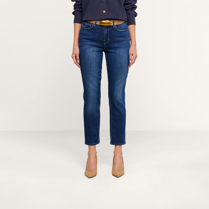 A person wearing the Celestia Slim-Leg Jean, a dark long-sleeve shirt, a brown belt, and tan high-heeled shoes stands against a plain white background.