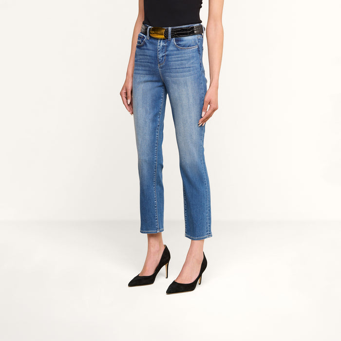A person wearing the Celestia Slim-Leg Jean in light blue—a high-rise, cropped skinny fit made from stretch denim—paired with a black sleeveless top, a black belt with a gold buckle, and black high-heeled shoes, standing against a plain white background.