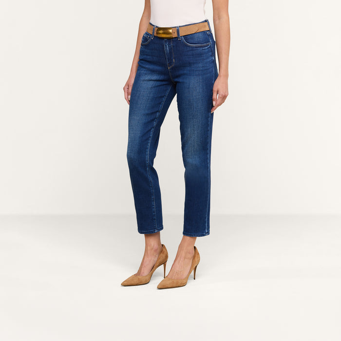 A person wearing the Celestia Slim-Leg Jean, styled with a brown belt, a white top, and tan high heels, stands against a plain white background. Only the lower half of the body is visible.