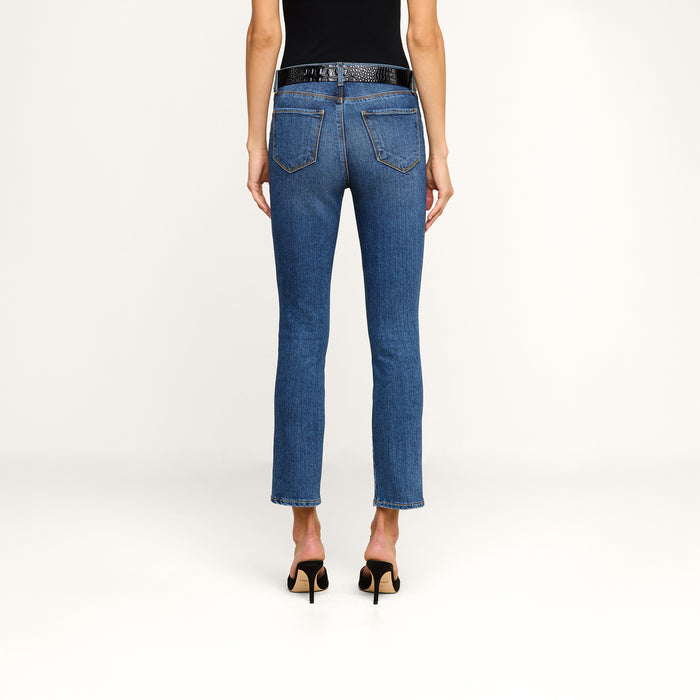 Woman standing with her back to the camera, wearing a black top, blue Celestia Slim-Leg Jean made from stretch denim, a black belt, and black high-heeled shoes, against a plain white background.