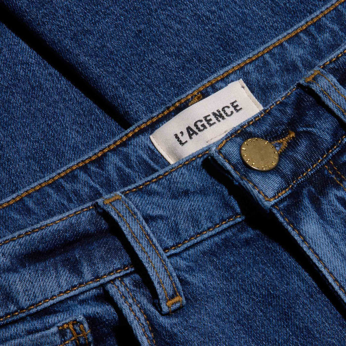 Close-up of Celestia Slim-Leg Jean in blue stretch denim, featuring a metal button, belt loops, and a white fabric label with the brand name LAGENCE sewn into the ultra high rise waistband.