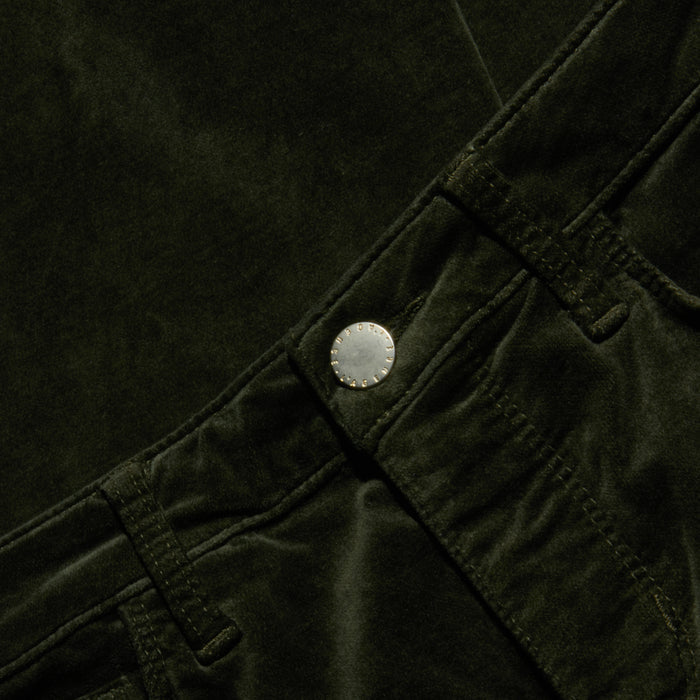 Close-up of the Celestia Velvet Slim-Leg Jean in dark green, featuring the waistband, belt loops, and metallic button, with emphasis on the texture and details of the stretch velvet fabric and stitching.
