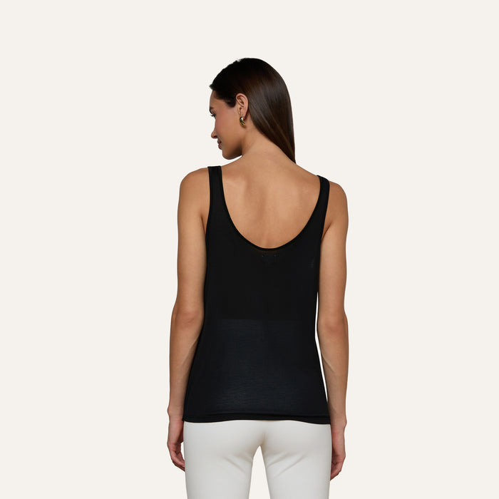 Wearing the Celia Scoopneck Tank in black, a person with straight brown hair and white pants stands with their back to the camera against a plain light background.