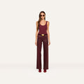 A woman wearing sunglasses, a sleeveless burgundy top, the Clayton Coated Wide-Leg Jean with a contoured waistband and belt, and matching shoes stands against a plain white background.