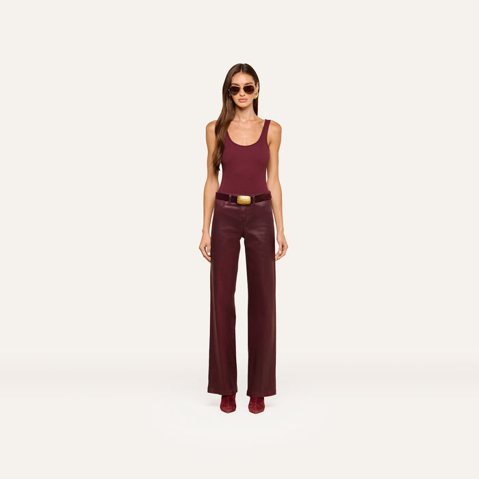 A woman wearing sunglasses, a sleeveless burgundy top, the Clayton Coated Wide-Leg Jean with a contoured waistband and belt, and matching shoes stands against a plain white background.