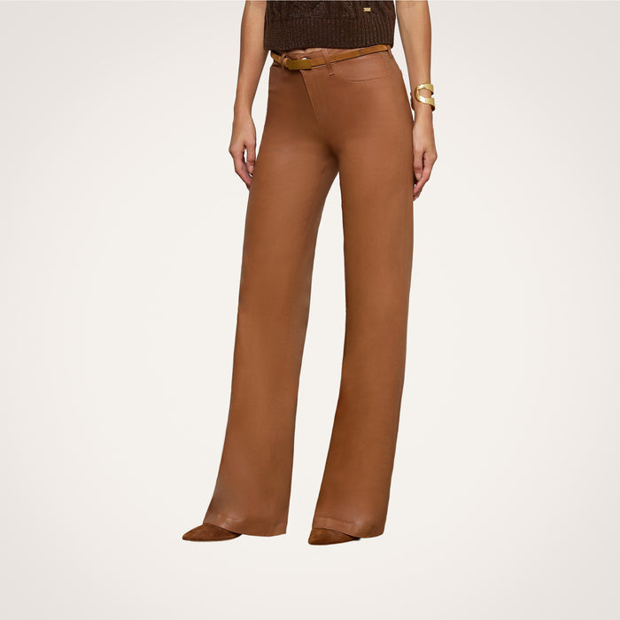 A person shown from the shoulders down against a plain background wears the Clayton Coated Wide-Leg Jean, featuring a high-waisted fit and contoured waistband, paired with a dark sleeveless top, brown pointed shoes, and a gold bracelet.