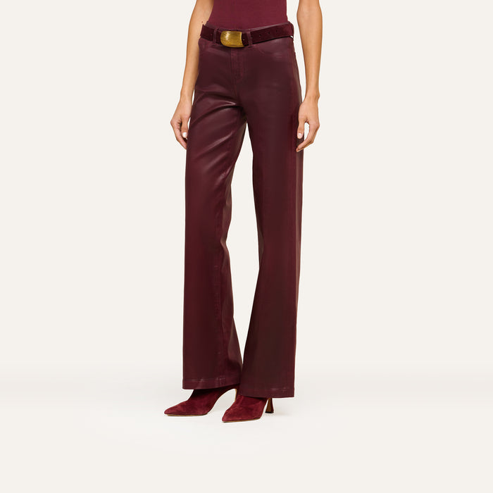 A person models the Clayton Coated Wide-Leg Jean, featuring a high waist, wide-leg silhouette, contoured waistband, and matching belt in burgundy leather. They pair the jeans with pointed burgundy heeled shoes. The top of their head is not visible.