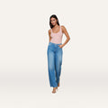 A woman poses against a plain white background wearing the Clayton Wide-Leg Jean—a high-rise, stretch denim style—in a pink tank top and heeled sandals, with one hand in her pocket.