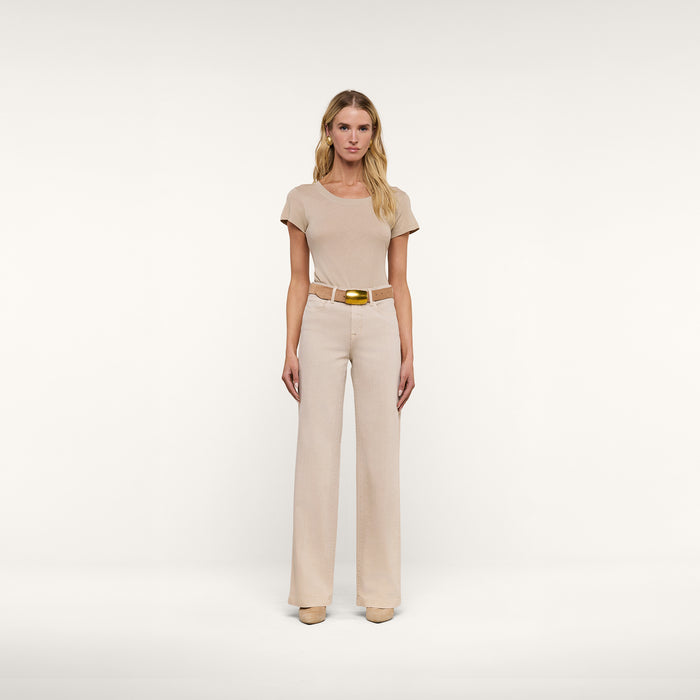 A woman stands facing forward, wearing a beige short-sleeve top, beige shoes, and the Clayton Wide-Leg Jean in a matching high-rise, tall wide-leg style with a belt, against a plain white background.