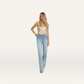 A woman with long blonde hair wears a cream satin camisole, heels, and the Clayton Wide-Leg Jean in a light wash high rise style, posing against a plain white background.