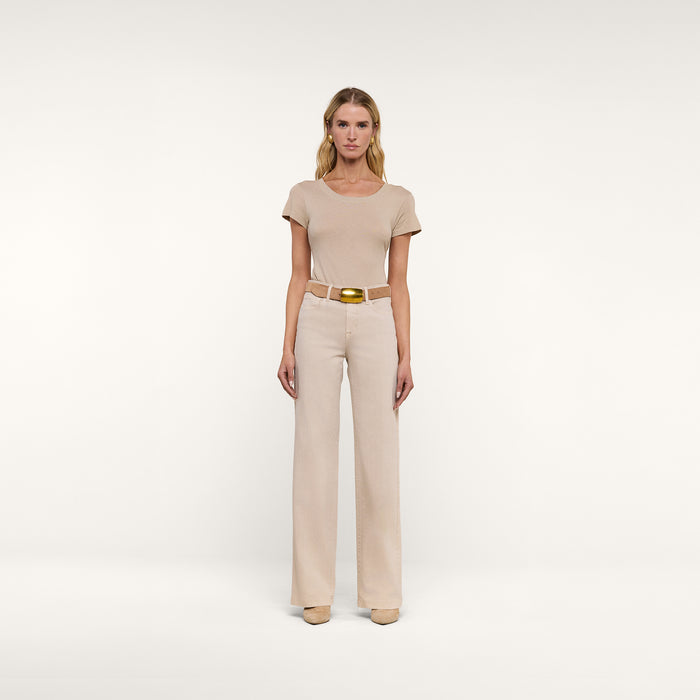 A woman stands facing forward in a beige short-sleeve top, the Clayton Wide-Leg Jean in stretch denim with a belt, and beige shoes, against a plain white background.