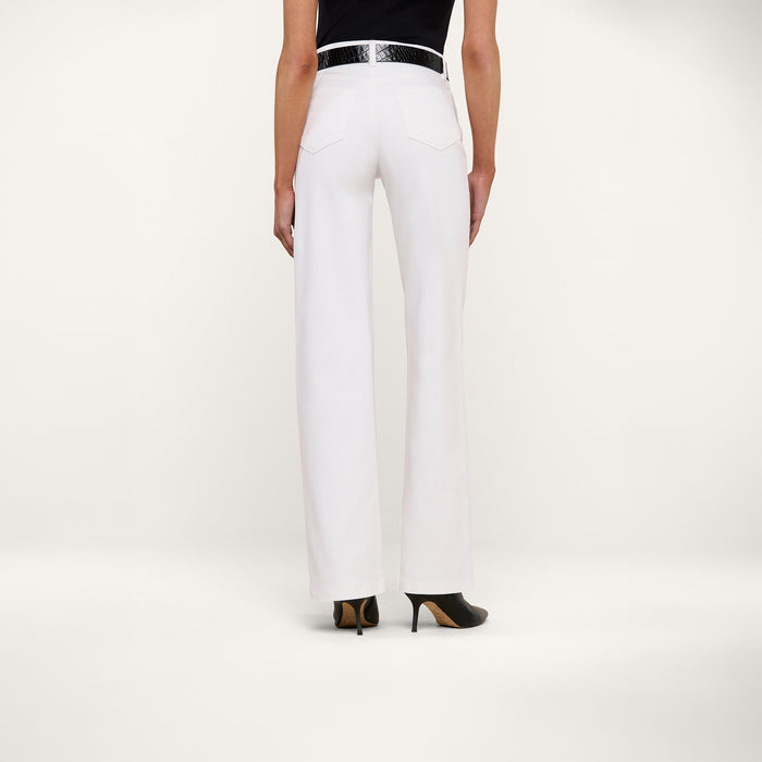 A person is shown from the back standing against a plain white background wearing the Clayton Wide-Leg Jean in white, styled with a black belt and black high heels.