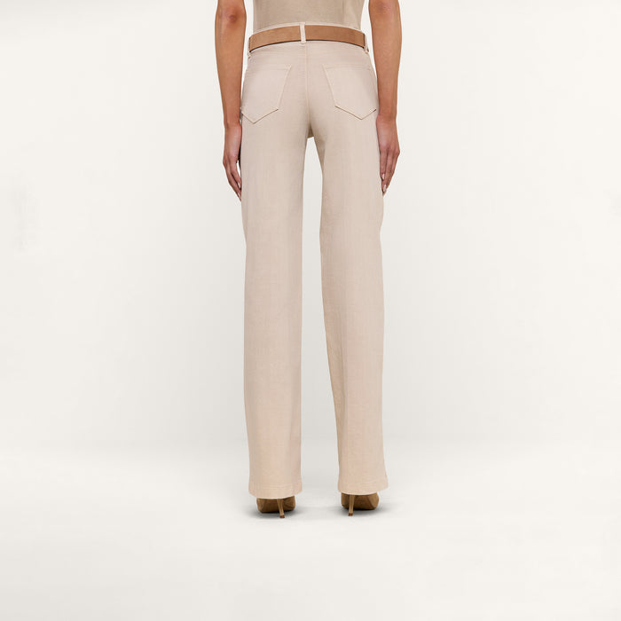 A person is shown from the back, displaying only the lower half of their body, dressed in beige Clayton Wide-Leg Jeans made from stretch denim with back pockets and a fitted waistband. The jeans are paired with a beige top and tan heeled shoes, set against a plain white background.