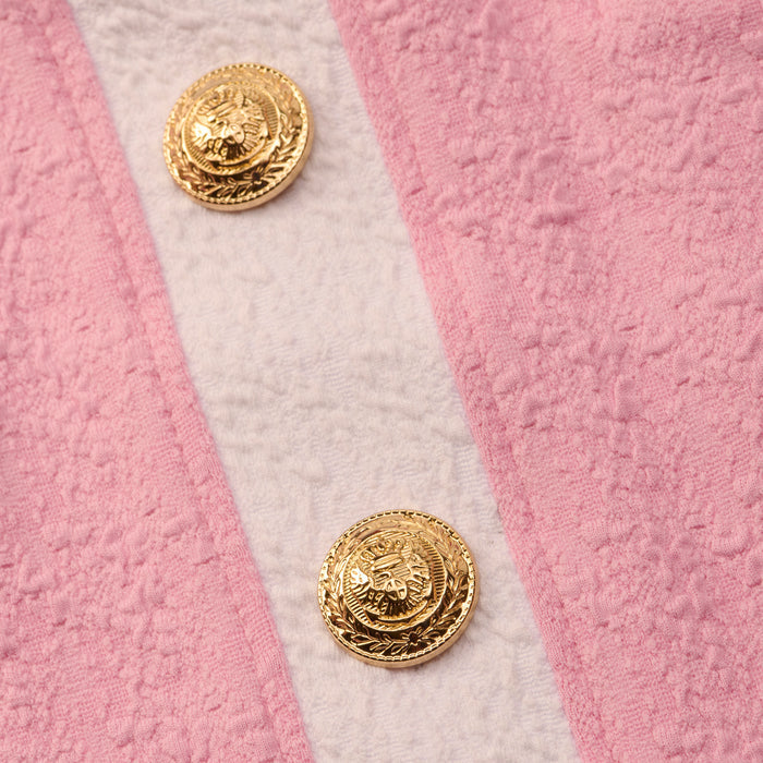Close-up of the Coco Mini Skirt Cover-Up, featuring two ornate gold buttons with an embossed design on textured bouclé in light pink fabric with a beige center.