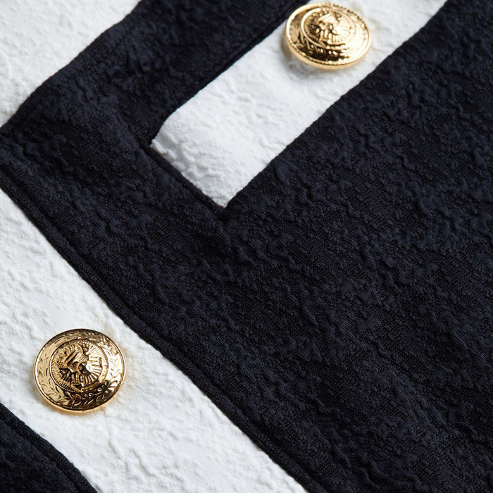Close-up of the Coco Mini Skirt Cover-Up’s textured bouclé fabric in black and white, accented with gold decorative buttons. The embossed design on the buttons adds a luxurious detail to the garment.