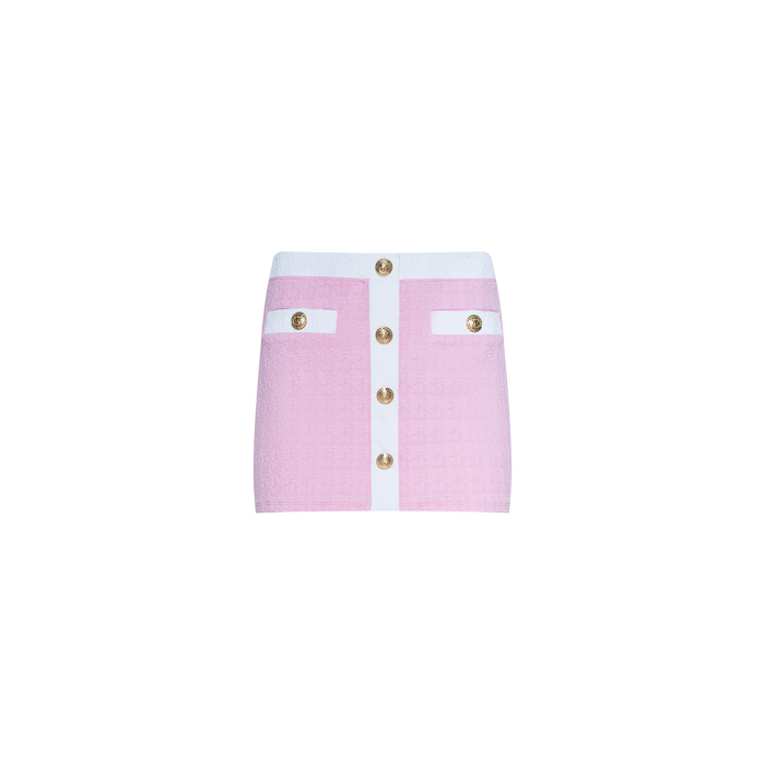 The Coco Mini Skirt Cover-Up is a pink textured bouclé mini skirt featuring a white waistband, a white vertical panel down the front, gold buttons along the center, and two front pockets each adorned with gold button details.