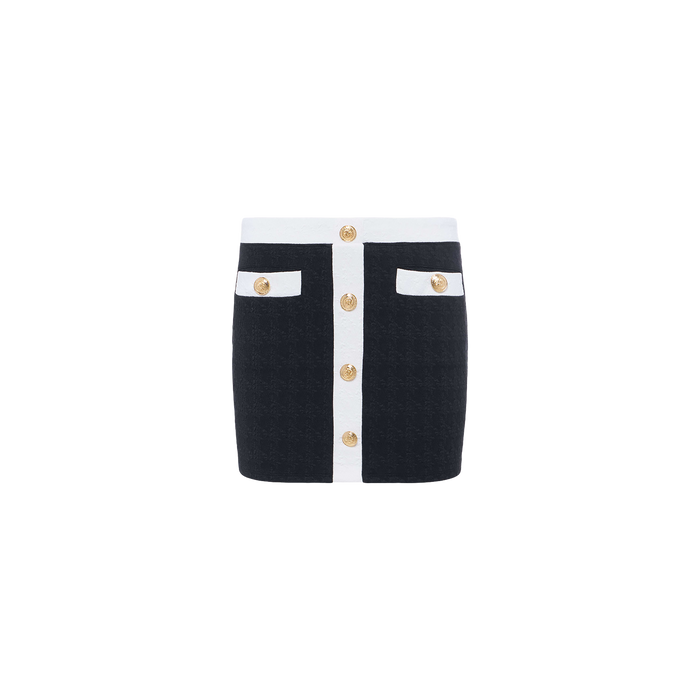 Introducing the Coco Mini Skirt Cover-Up: a black bouclé mini skirt featuring white trim, gold buttons down the front, and two front pockets accented with matching white trim and gold buttons—beautifully displayed on a plain white background.