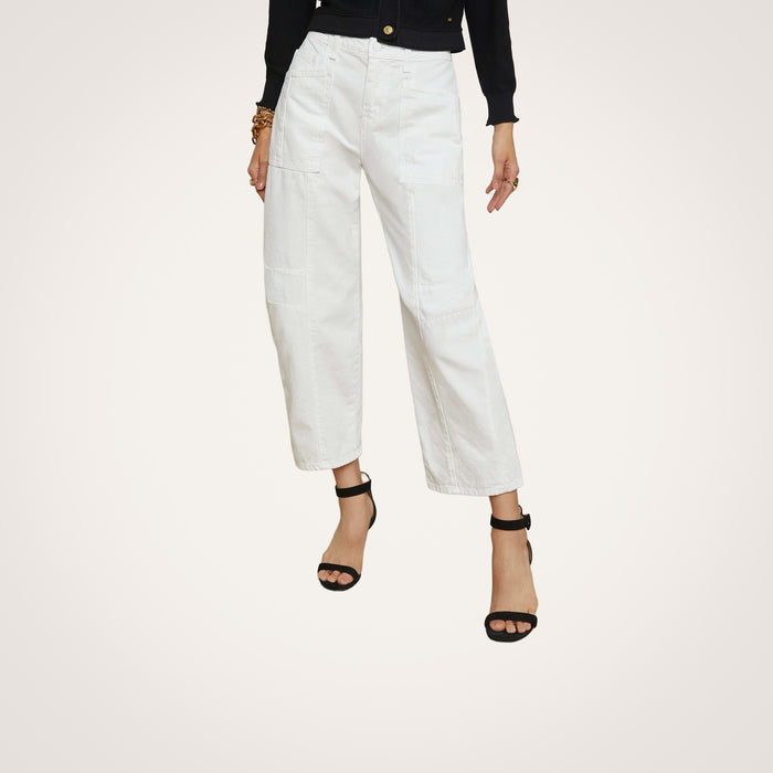 A person wearing the Cody Barrel-Leg Jean in a high-rise white denim style, paired with black heeled sandals, a black long-sleeve top, and bracelets, stands against a plain light background.