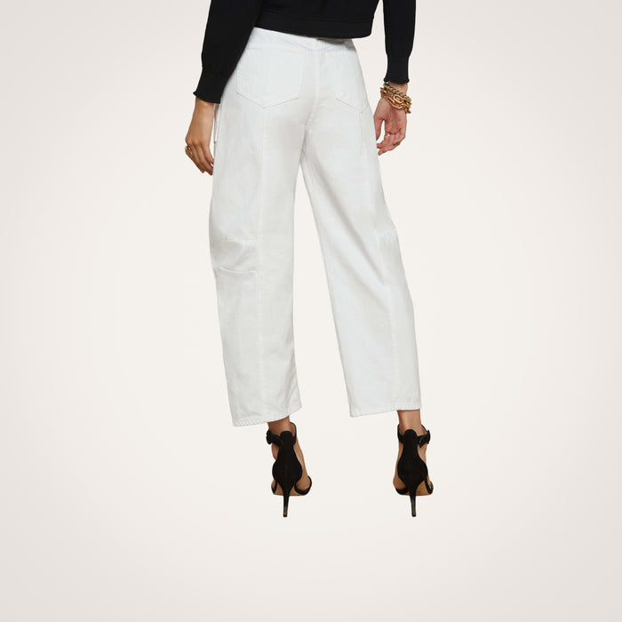 Wearing the Cody Barrel-Leg Jean in white, paired with black high-heeled sandals, a black long-sleeve top, and gold bracelets, this individual stands with their back to the camera against a plain light background.