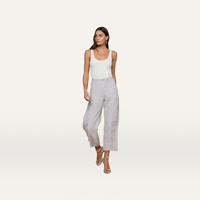 A woman wearing a white tank top, the Cody Cropped Linen Pant in light gray, and strappy sandals stands against a plain light background.