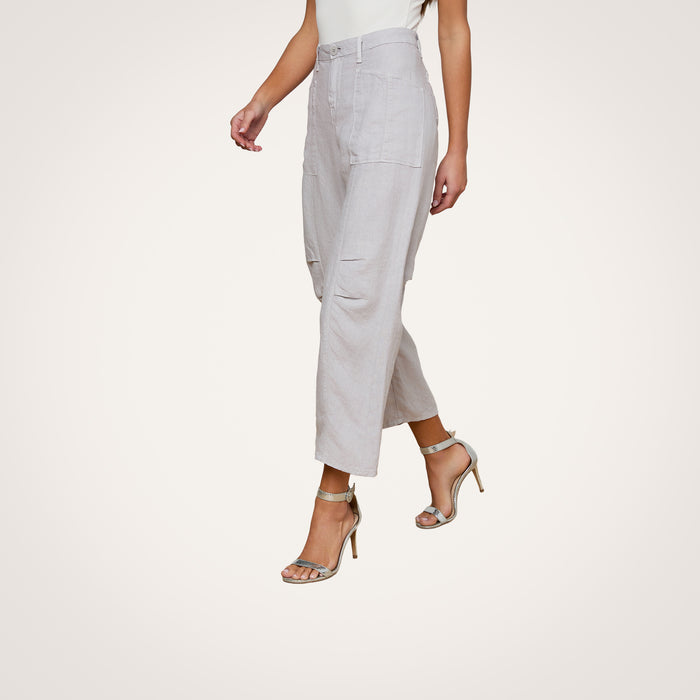 A woman is walking against a plain white background, wearing the Cody Cropped Linen Pant in light gray paired with a sleeveless white top and metallic high-heeled sandals. Her head is not visible.