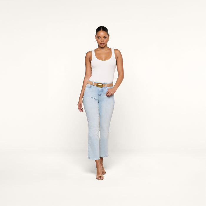 A woman in the Cole Scoopneck Tank and light blue jeans with heeled sandals stands against a plain white background, walking confidently toward the camera.