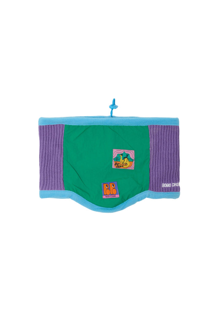 A colorful fleece neck warmer with green and purple panels, blue trim, and colorful illustration patches set against a white background