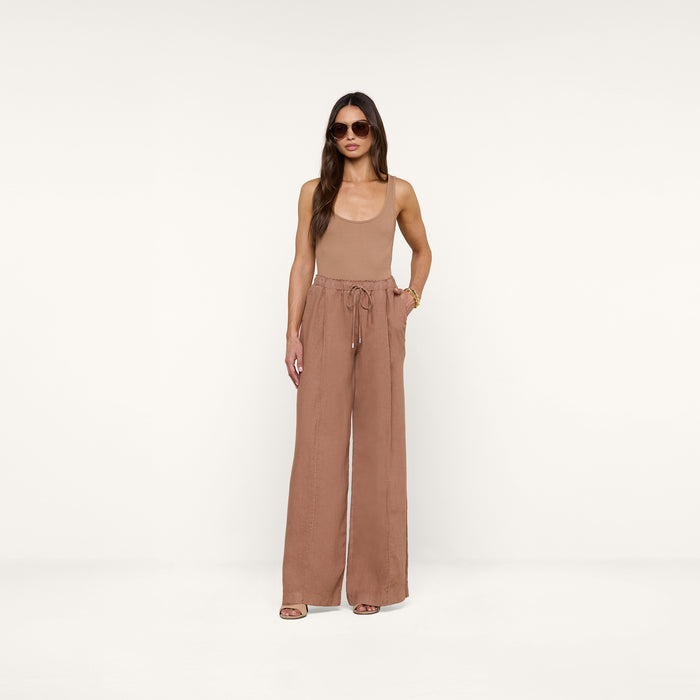 A woman wearing sunglasses, a sleeveless tan top, and the Connie Linen Drawstring Trouser—high-waisted, wide-leg vacation pants with a drawstring waistband—stands against a plain white background.
