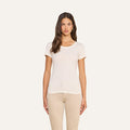 A woman with long brown hair stands facing forward against a plain light background, wearing the Cory Cotton Scoopneck Tee in vintage off-white—a short-sleeve, ultra-soft cotton classic—paired with beige pants.