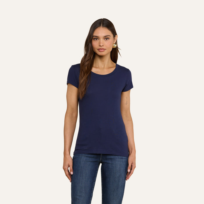 A woman stands facing forward, wearing a navy Cory Cotton Scoopneck Tee paired with blue jeans against a plain light background.