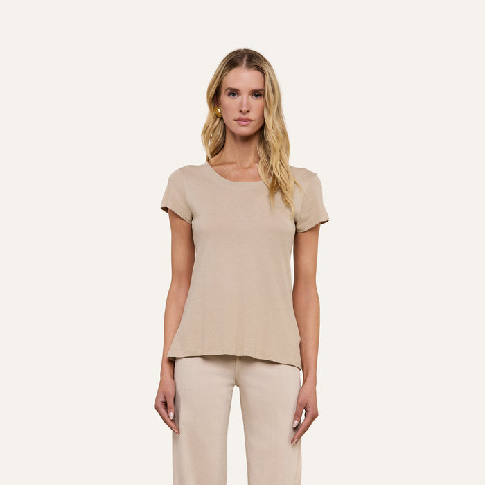 A woman with long blonde hair faces forward, wearing the Cory Cotton Scoopneck Tee in taupe and light-colored pants, set against a plain beige background.