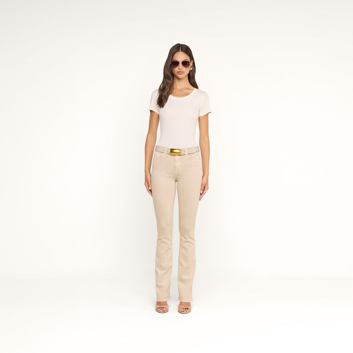 A woman with long hair wearing sunglasses, the Cory Cotton Scoopneck Tee in an off-white shade, beige pants with a belt, and sandals stands against a plain white background.
