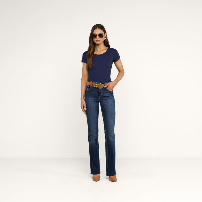 A woman wearing sunglasses, a navy Cory Cotton Scoopneck Tee crafted from ultra-soft cotton, blue jeans with a brown belt, and tan high heels stands against a plain white background.