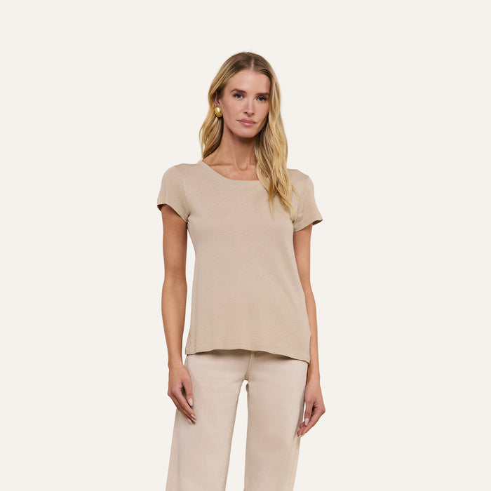 A woman with long blonde hair wears the Cory Cotton Scoopneck Tee in slim fit taupe and light pants, standing against a plain beige background. She faces forward, relaxed, with her hands at her sides.