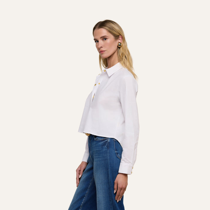 Woman with long blonde hair wearing the Cosette Shirt, a tailored white button-up, and blue jeans, standing against a plain light background and facing slightly to the side.