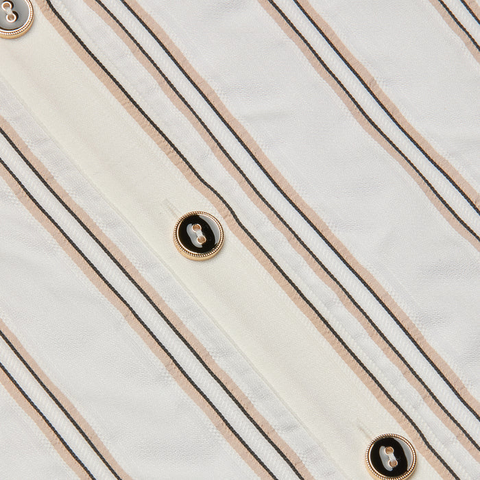 Close-up of the Cosette Shirt, crafted from white fabric with vertical beige and black jacquard stripes and accented by gold-rimmed black buttons sewn along the stripes, evoking a tailored look.
