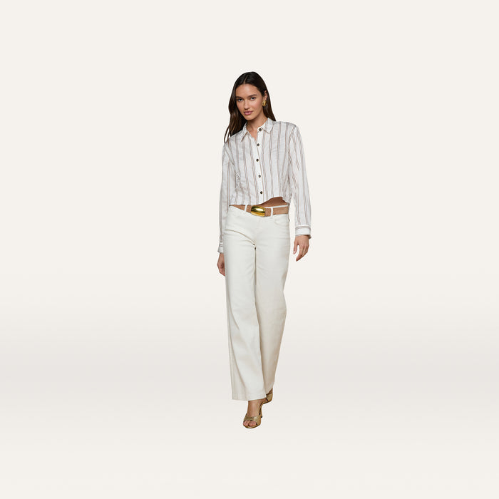 A woman wearing the Cosette Shirt with jacquard stripes, white wide-leg pants, a gold belt, and sandals stands against a plain white background. She has straight dark hair.