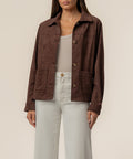 Chocolate brown faux suede jacket with collar, button front, and patch pockets worn over white top.