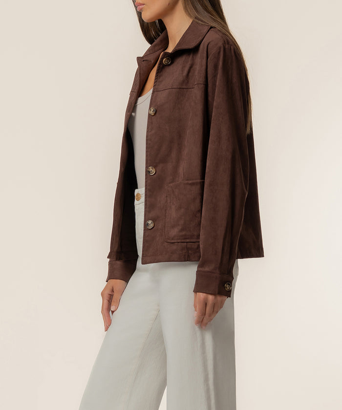 Woman wearing chocolate brown faux suede jacket with collar and button front over cream pants.