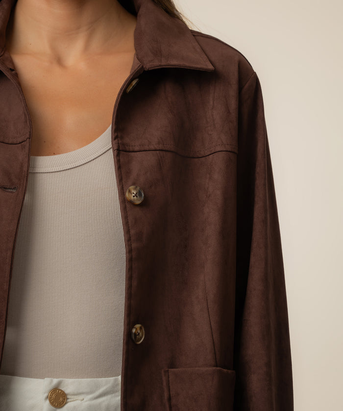 Brown faux suede jacket with collar and horn buttons, worn open over cream ribbed top.