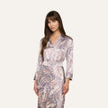 Woman with long brown hair wearing the Dani Silk Blouse, featuring a pastel abstract pattern reminiscent of butterfly wing print, standing against a plain light background.