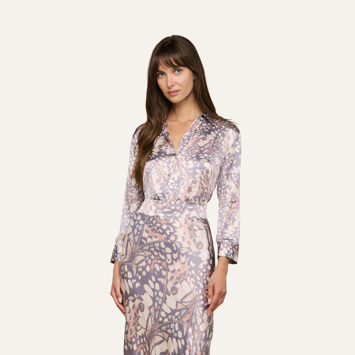 Woman with long brown hair wearing the Dani Silk Blouse, featuring a pastel abstract pattern reminiscent of butterfly wing print, standing against a plain light background.