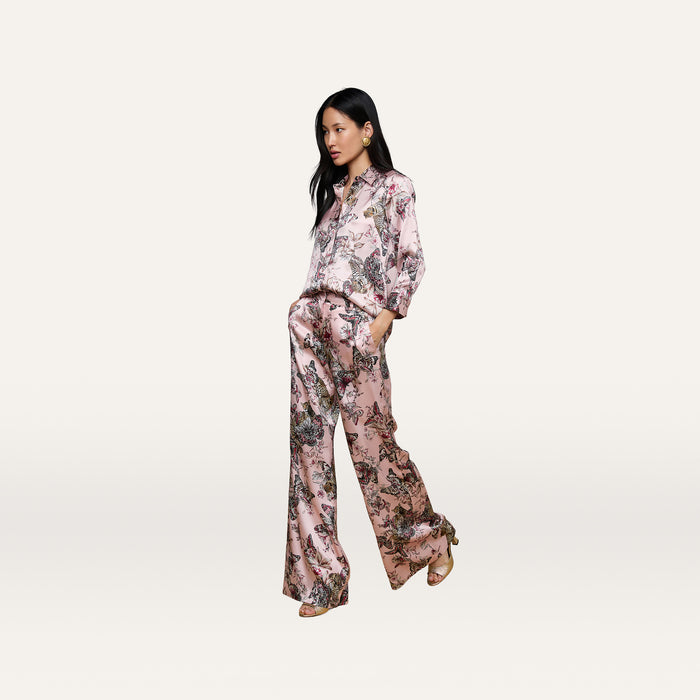 A woman stands and looks to the side, wearing the Dani Silk Blouse in a matching pink floral pajama-style set with wide-leg pants and tan high-heeled sandals, against a plain white background.