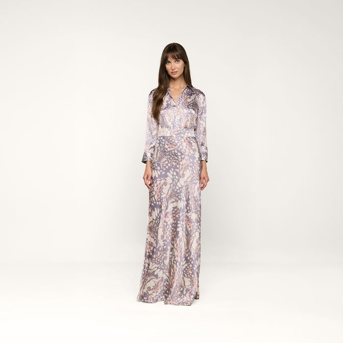 A woman stands against a plain white background, wearing the Dani Silk Blouse—a long-sleeved top with a relaxed fit and v-neckline, adorned with a delicate butterfly wing print in light purple tones.