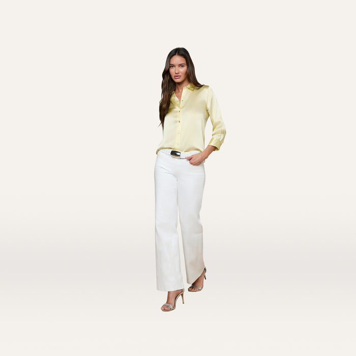 A woman wearing the Dani Silk Blouse in yellow, paired with white wide-leg pants and beige heeled sandals, stands against a plain white background.