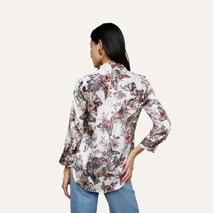 A woman is shown from the back wearing a white Dani Silk Blouse with a colorful butterfly jungle print and blue jeans, standing against a plain light background.