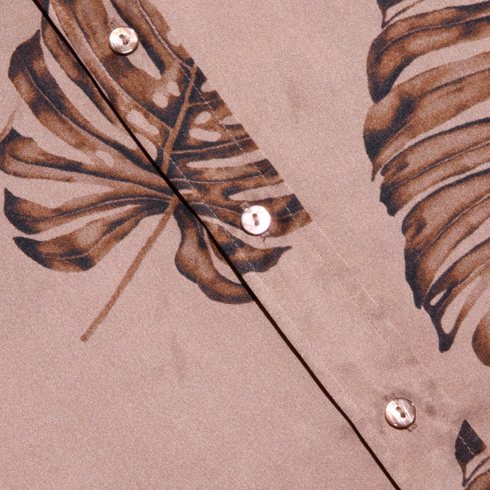 Close-up of the Dani Silk Blouse in beige, featuring a brown palm leaf print and pearl-like buttons. The smooth silk fabric and bold, tropical-inspired design give this button-down a distinctive look.
