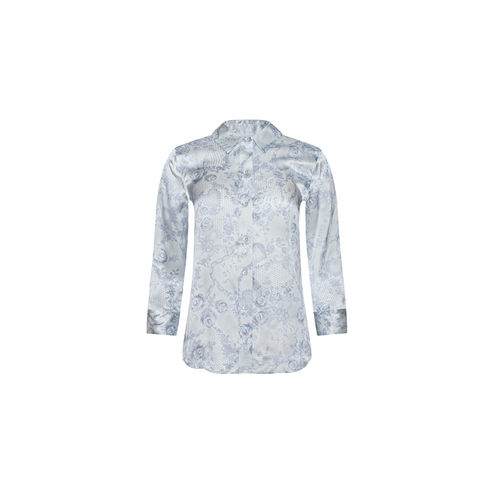 The Dani Silk Blouse is a light blue, long-sleeve button-down top crafted from silk, showcasing a subtle floral jacquard pattern with delicate ivory and blue lace accents and a pointed collar, displayed on a plain white background.